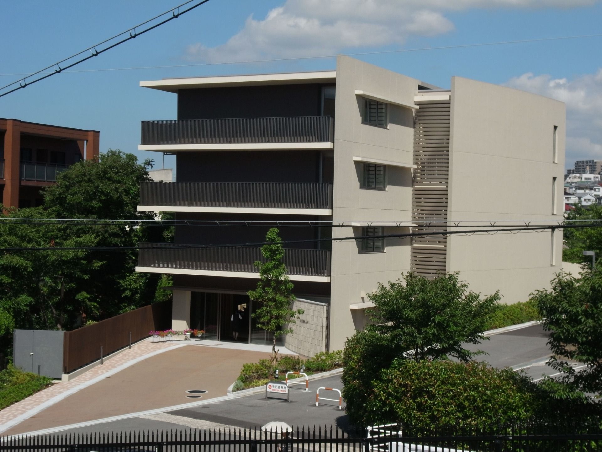 4階建ての緑に囲まれた建物。ベランダが付き、周辺には駐車場もある。