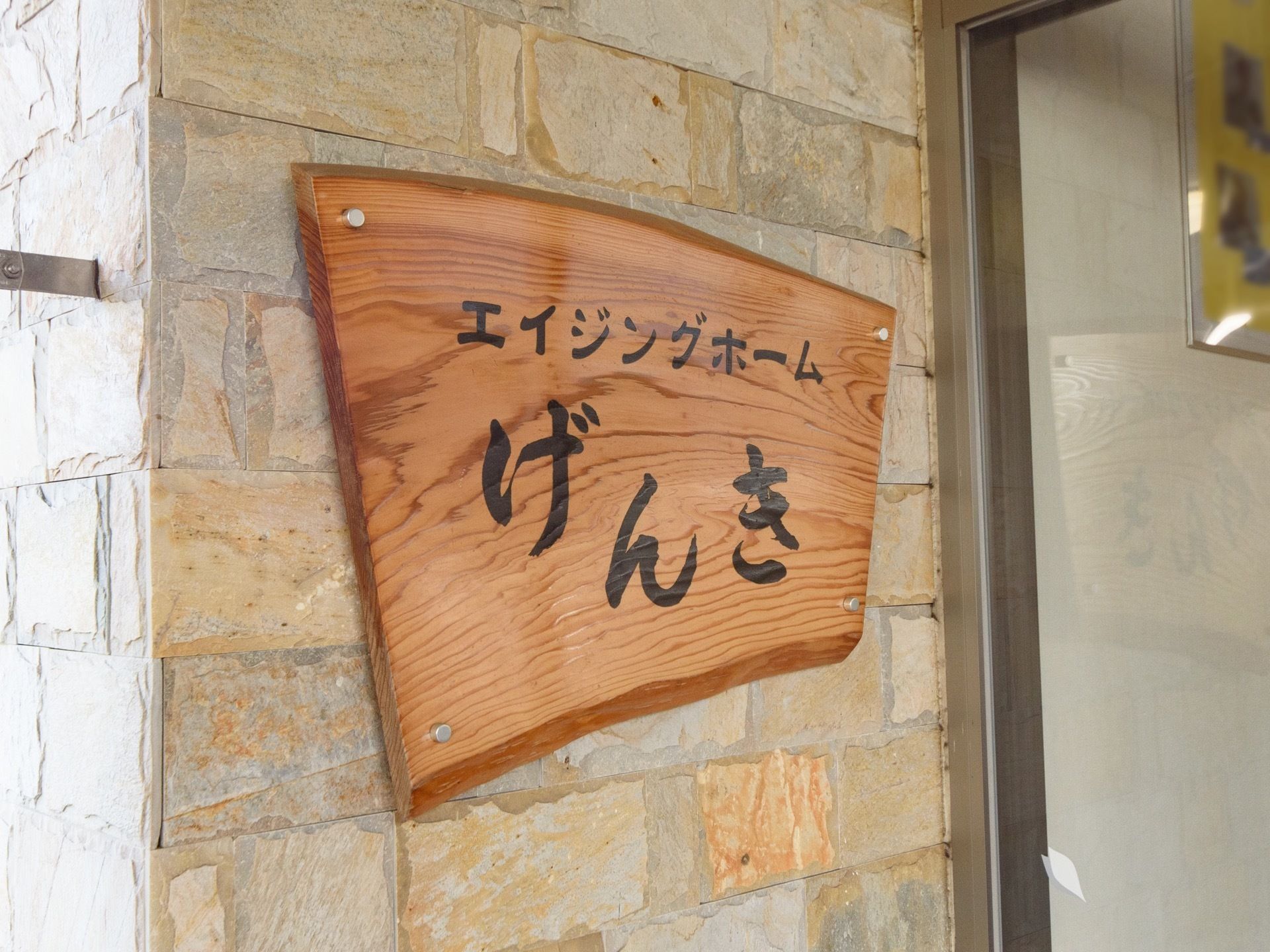 扇のような形の木の板で作られた看板が、玄関の横の壁に取り付けられている。ホームの名称などが黒色の文字で書かれている。