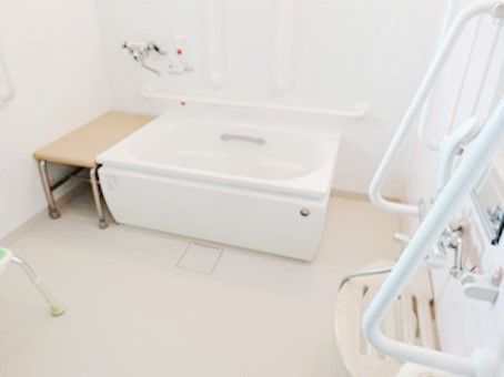 ベンチ付きの浴槽は白く、浴槽やシャワー周辺には手すりもたくさんついている。