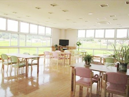 壁一面が窓となっている開放的なリビング。4人掛けのテーブルが複数並び、テレビもある。