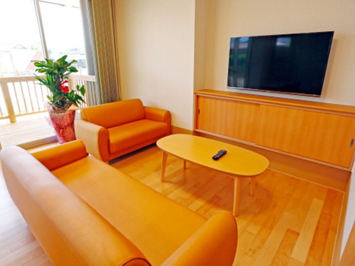 大型の壁掛けテレビが設置された談話スペース。オレンジのソファの応接セットが置かれ、観葉植物も飾られている。