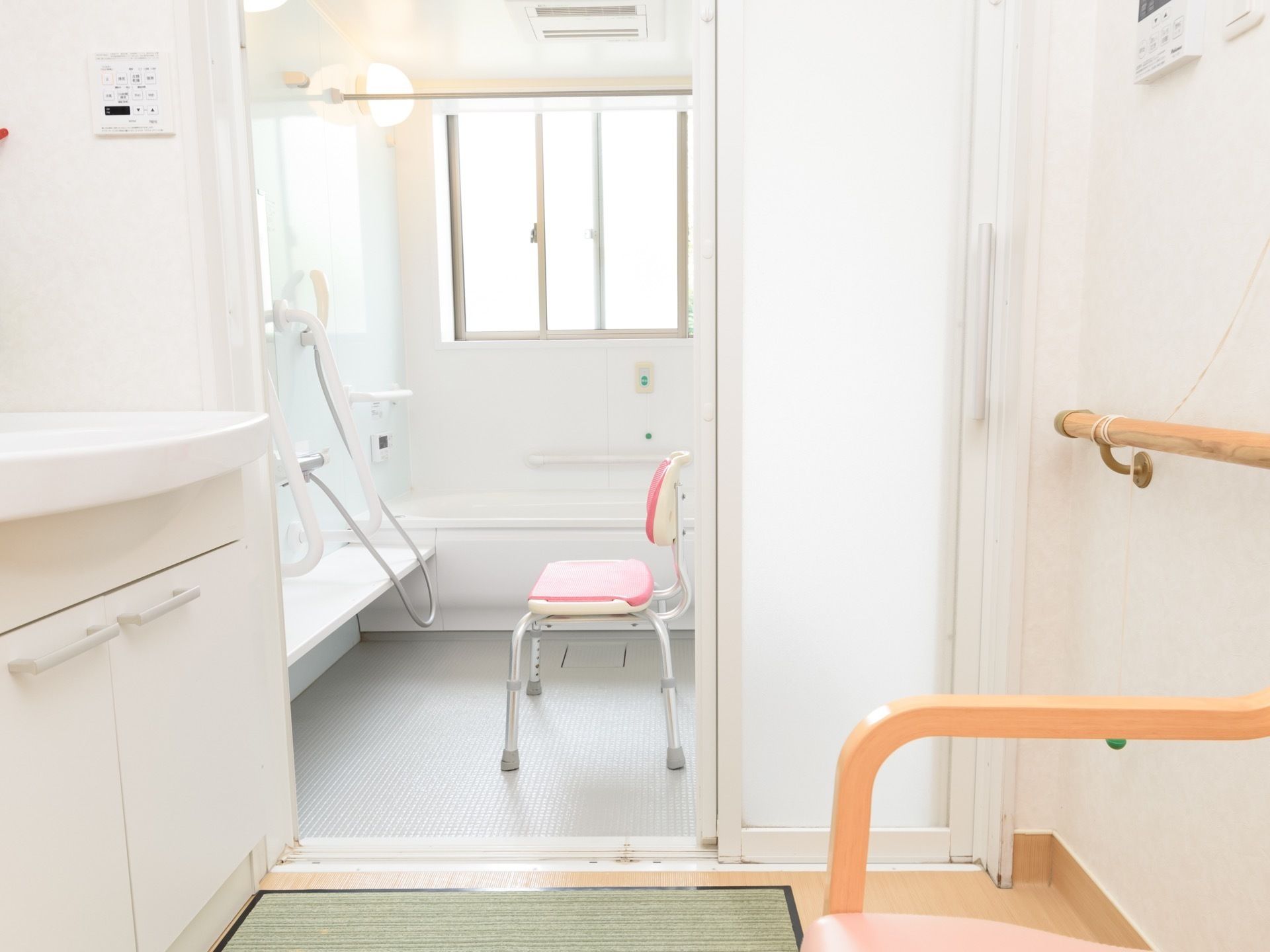 浴室に、ピンク色の座面と背もたれがついた椅子が置かれている。脱衣所には、足ふきマットが敷かれている。