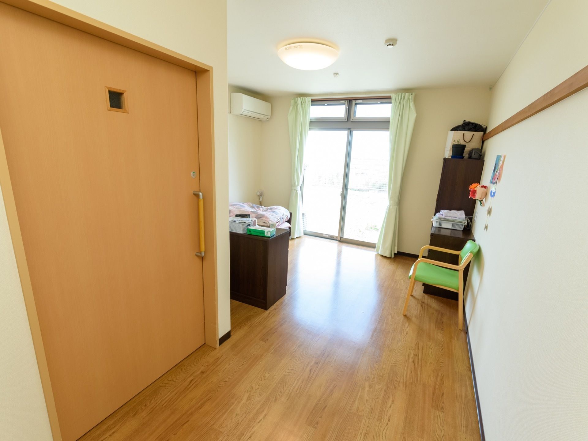 居室には掃き出し窓がある。その左側の壁の上部にエアコンが設置されている。入口付近には、大きな取っ手がついた引き戸がある。