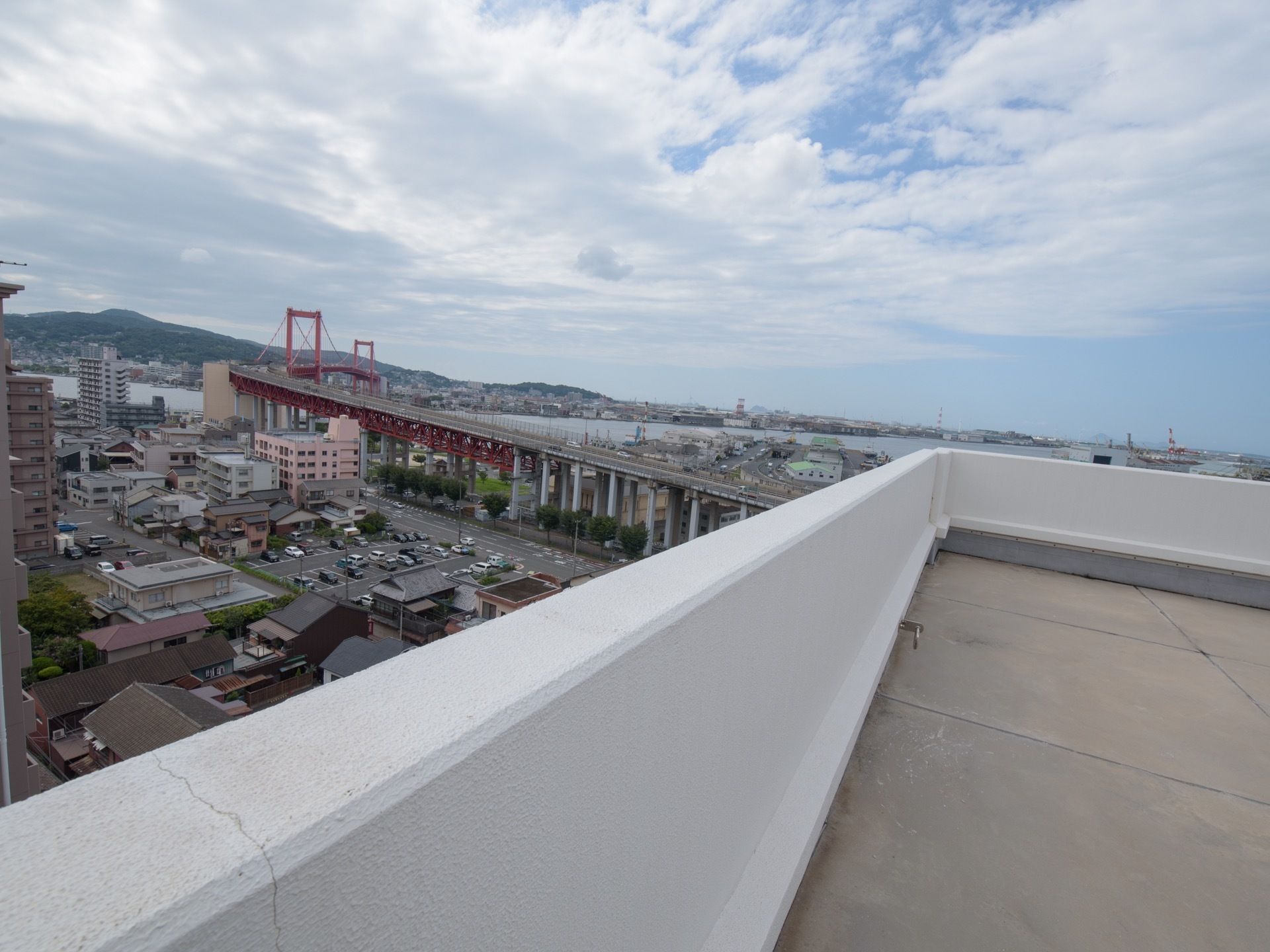 施設のベランダからは、周辺の景色が一望できる。道路が川に架かる橋に繋がっている風景や近くに高層マンション、駐車場などがある様子もよく見える。