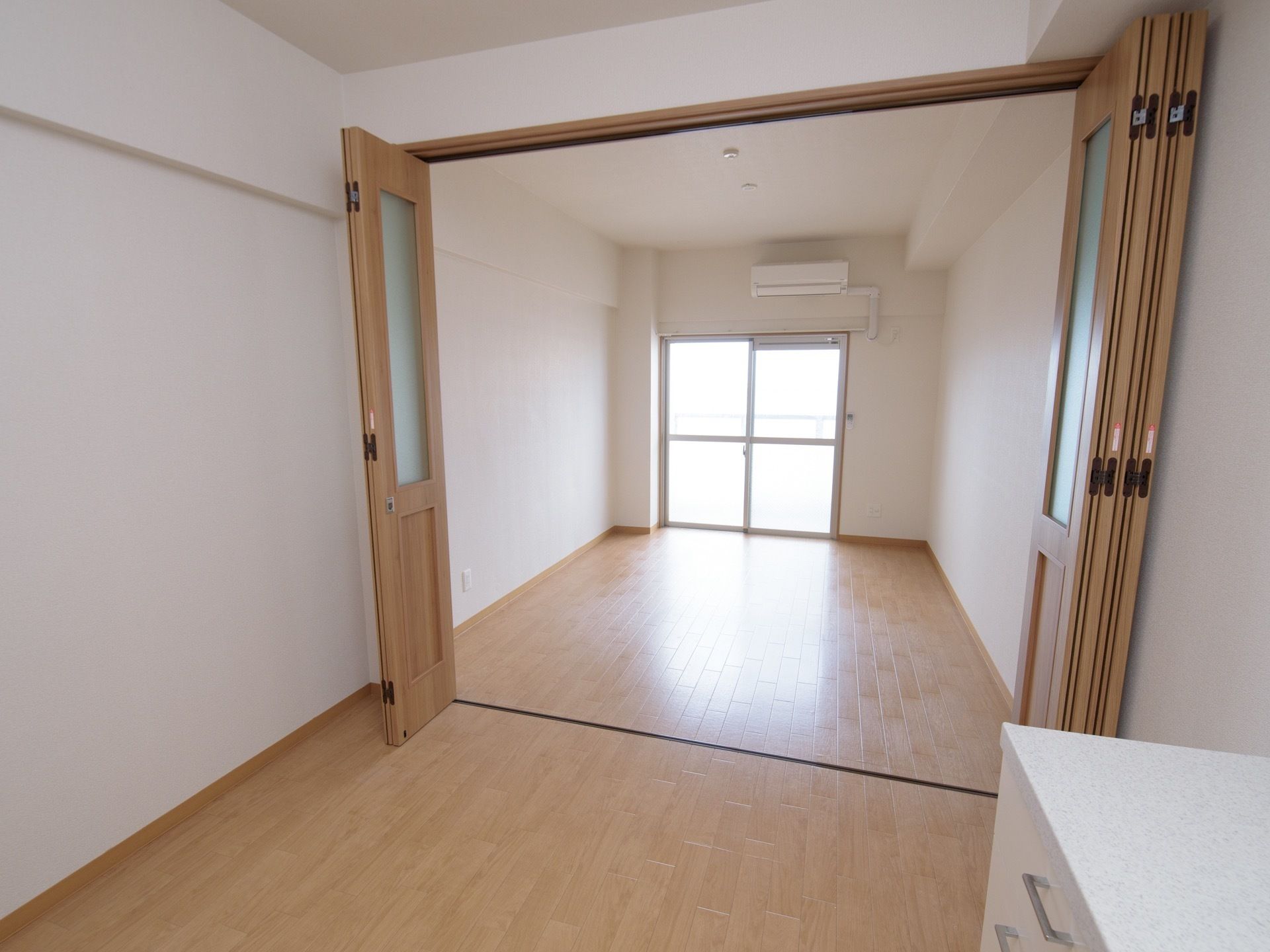 居室には、縦長に広い居住空間を、２部屋に仕切る間仕切り扉がある。正面は、ガラス戸になっており上部の壁面にエアコンが付いている。