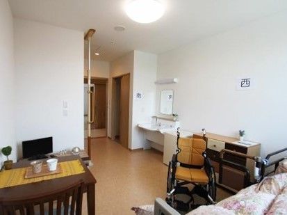 車いすと調度品類が並んでいる施設内の居室の様子。手前に介護用ベッドが置いてあるスペース