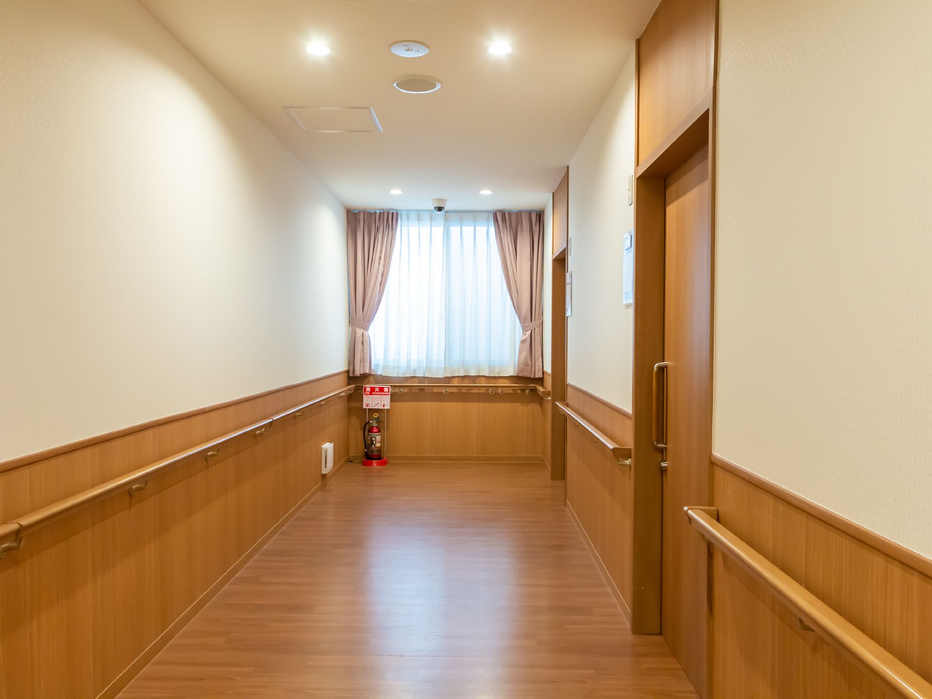 車いすの高齢女性のそばにはピンクのエプロンを付けた女性スタッフがいて、女性に寄り添いながら笑顔で過ごしている。