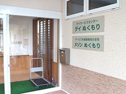 自動ドアが設置された玄関には住宅名と併設の事業所名が書かれたプレートが飾られ、ポストも付いている。