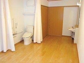 カーテンで開け閉めするタイプのトイレが設置され、車いす対応の洗面所も付いたフローリングの部屋。