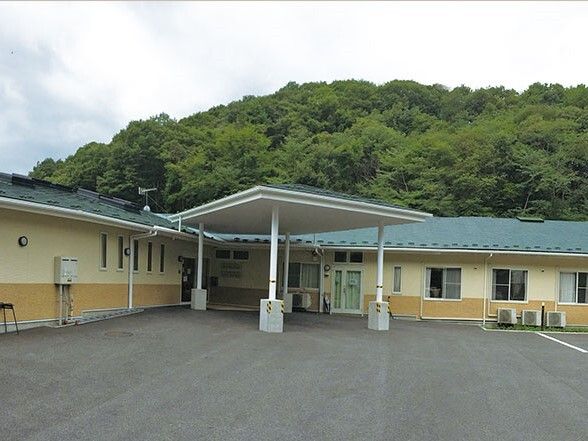 緑に囲まれた豊かな環境の中に立っている平屋建ての建物には緑の屋根が付いている。広い駐車場もある。