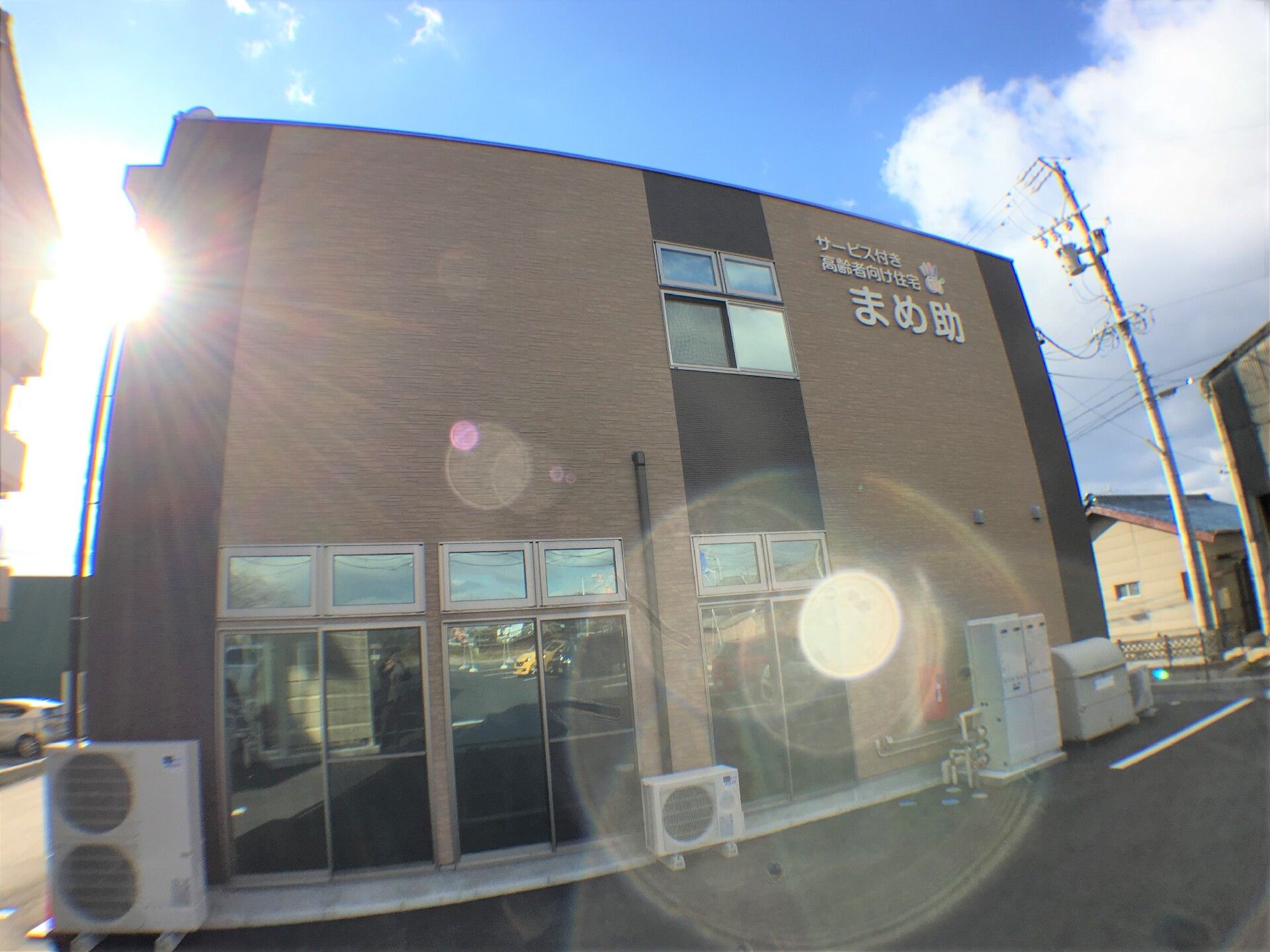 二階建てで窓がたくさんついた施設外観。後ろから太陽の光に照らされている