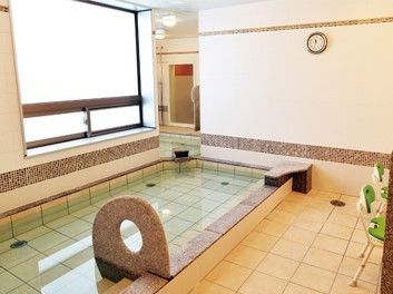 大浴場には広い浴槽があり、大きな窓が付いている。シャワーの前にはグリーンのシャワーチェアがある。
