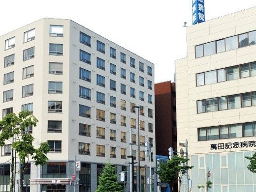 オフホワイトの大きな建物が二つ並んでいる。右側がグループ内の病院、左側が住宅。
