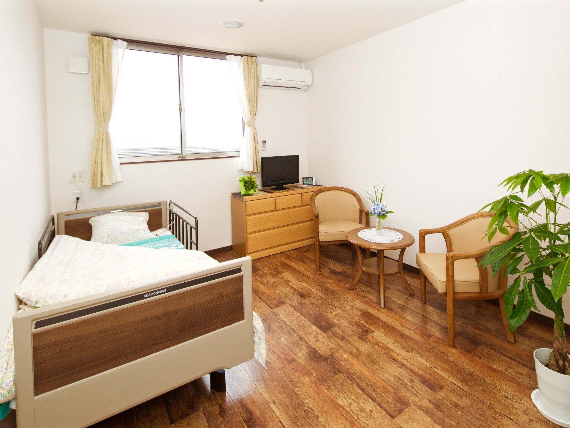 大きな窓があり明るい雰囲気。居室には、ベッドや家具、観葉植物だけでなくエアコンもついている。