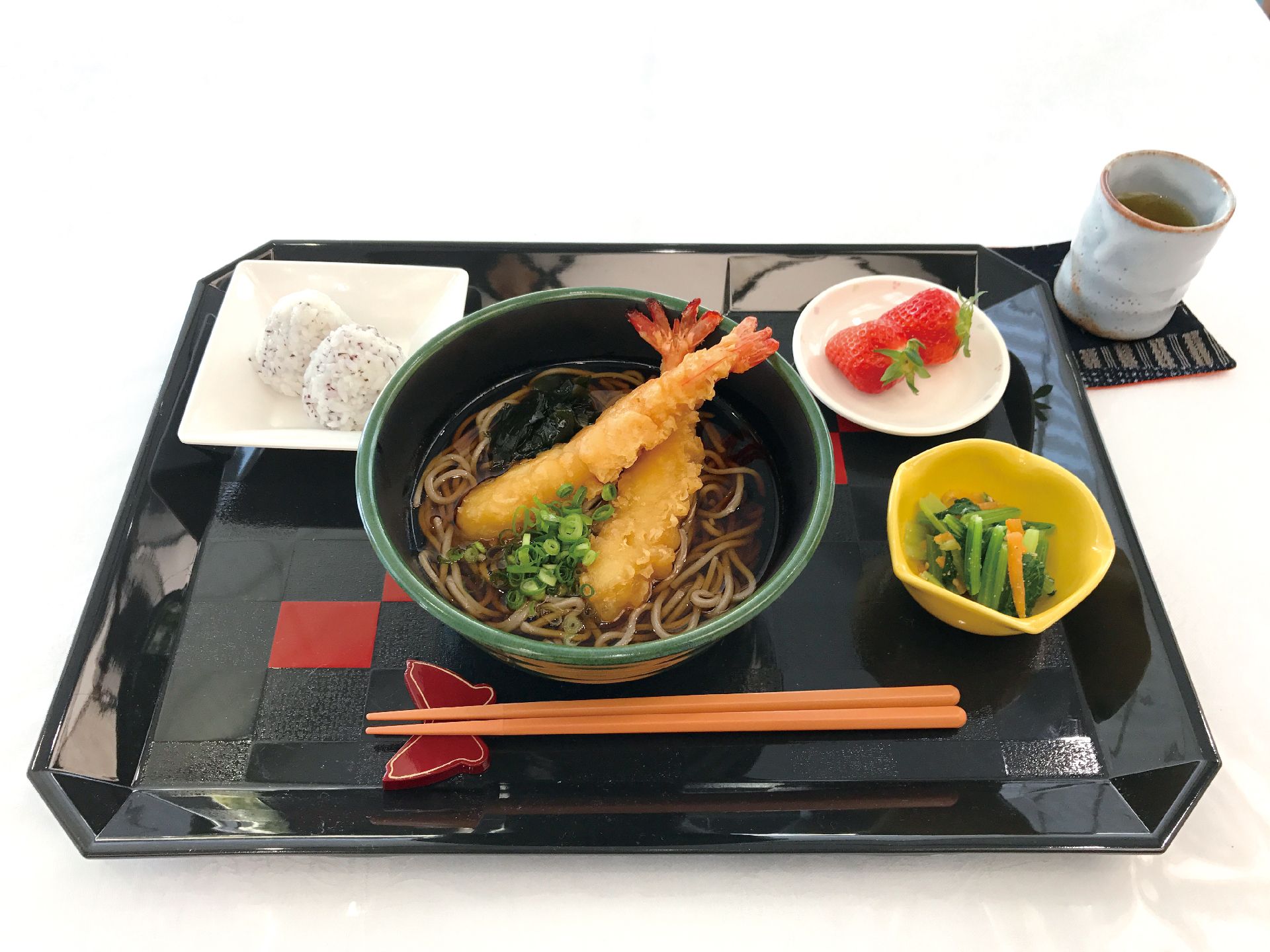 海老てんぷらが乗ったそばとおかず、デザートが乗っているメニュー