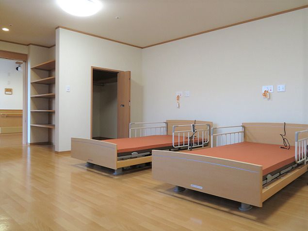 オレンジの介護ベッドが二つ並んだ広い部屋。居室の出入り口には収納棚があり、ベッドの近くにはクローゼットがあり、緊急通報装置も付いている。