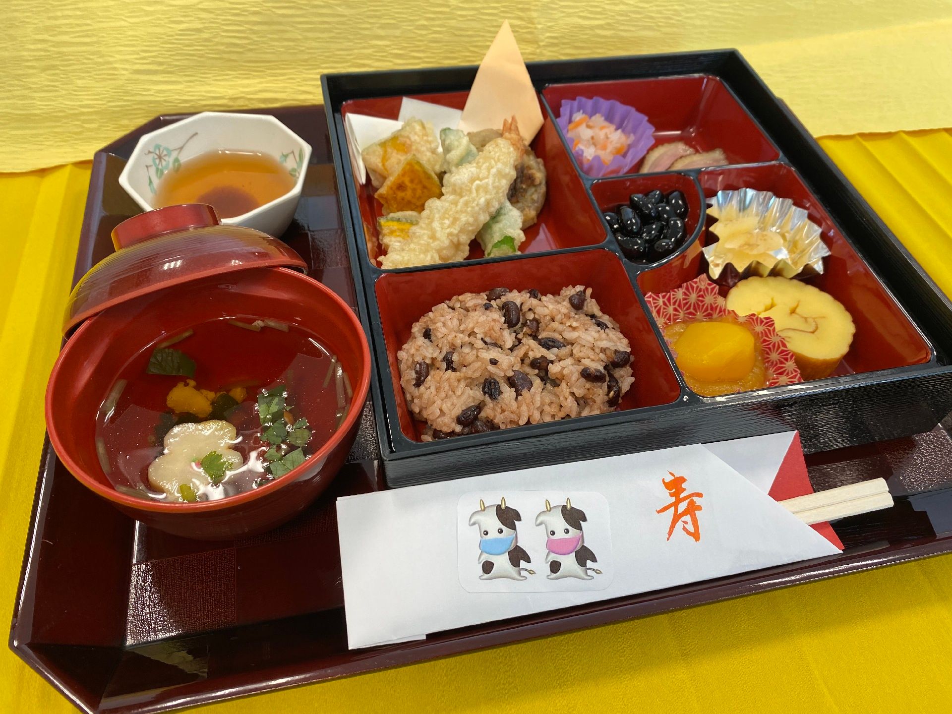 天ぷらの盛り合わせにちらし寿司、吸い物に天つゆ、いちごとオレンジなどが並べられた黒いトレー。それぞれデザインの異なる器に盛られ、お品書きも添えられている。