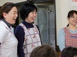 エプロンやポロシャツを身につけた女性スタッフたちが笑顔で何かを鑑賞している。