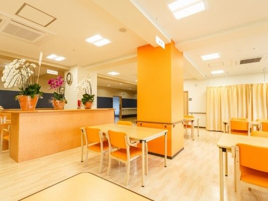 オレンジの壁やダイニングテーブルがよく目立つ明るい雰囲気のリビングダイニング。花も飾られている。