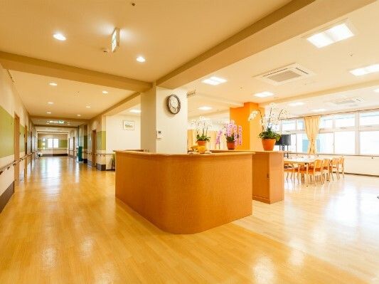 右側にはリビングダイニングがあり、観葉植物もたくさんある。左側にはまっすぐな廊下があり、手すりも付いている。