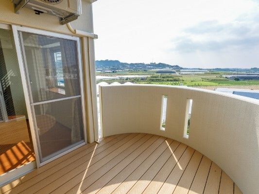 ウッドデッキが敷かれたバルコニーが居室から行き来ができるようになっている。日当たりがよく、周辺には緑が多い。