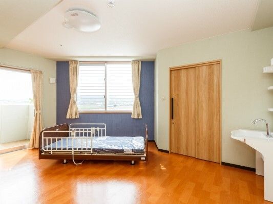 車いす対応の洗面所が付いたフローリングの部屋には大小の窓が付き、明るい雰囲気。介護ベッドもある。