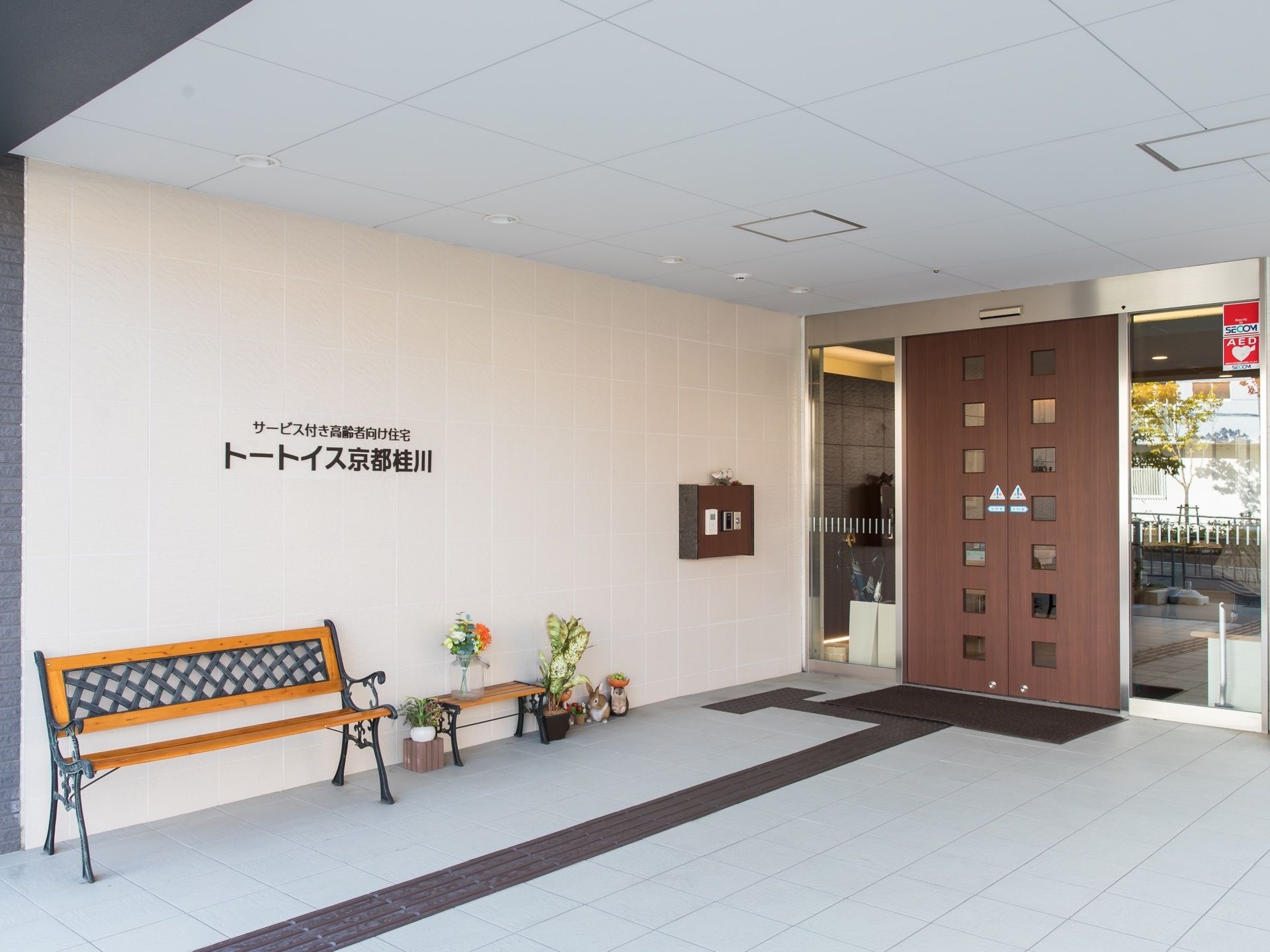 玄関には屋根がついている。ベンチがあるので待ち合わせ場所にもなる。間口の広い自動ドアでスムーズに出入りできる。