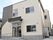 ベージュの2階建ての建物にブラックのラインが入っている。玄関先には黒い屋根も付いている。