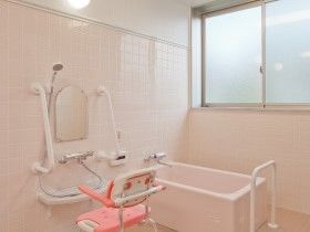 個浴やシャワーチェア、シャワーが設置されたピンク色の浴室。