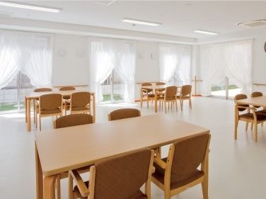 木製のダイニングテーブルが置かれ、ぬくもりが感じられる館内。窓にはレースカーテンが付いている。