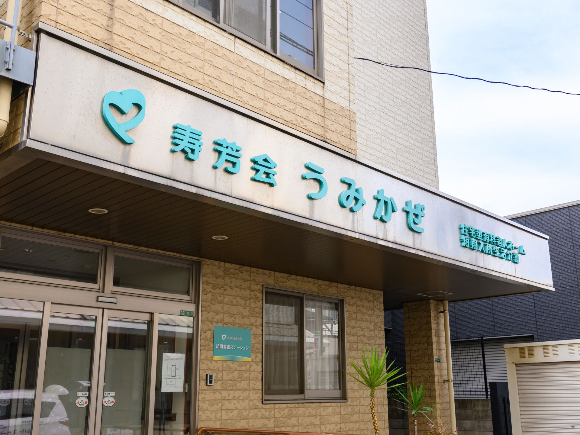 眼鏡をかけた車いすの高齢男性に白いゆったりとした服を着た高齢女性が寄り添い、笑顔で話している。