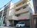 自動販売機が玄関先に置かれた4階建ての建物はベージュ系で建物の前には駐車スペースがある。