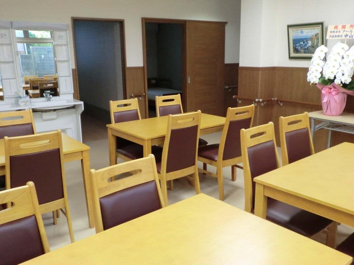 お祝いの欄の花や絵画が飾られた館内にはダイニングテーブルが複数置かれ、居室のドアは開いている。