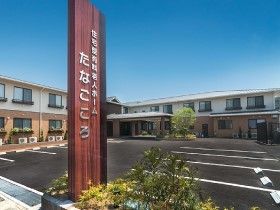 たなごころの看板が掲げてある様子。奥のほうに建物、その間に複数台並べられる駐車場がある
