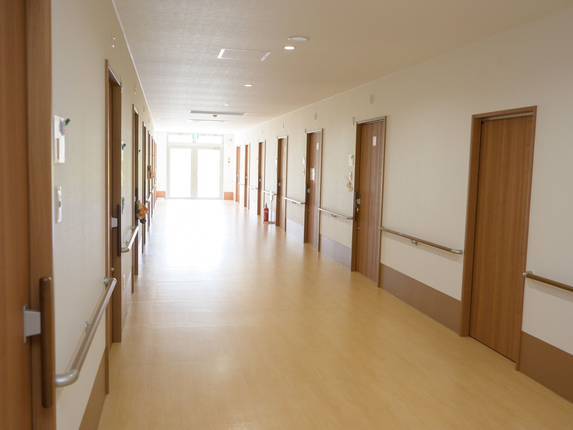 通路の両側には部屋の扉が並んでいて、壁には手すりが備えられている。扉の上に非常口の誘導灯がある。