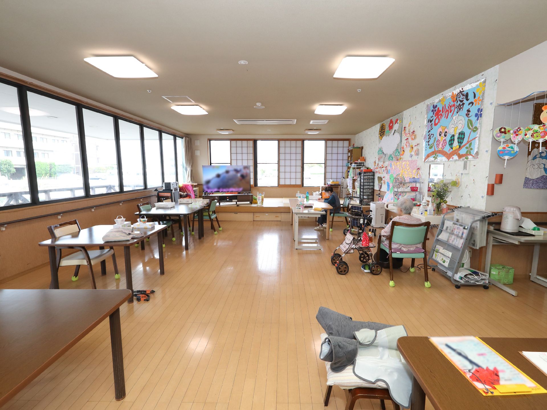 車椅子に座って手を振る高齢女性と介助をする女性ヘルパー