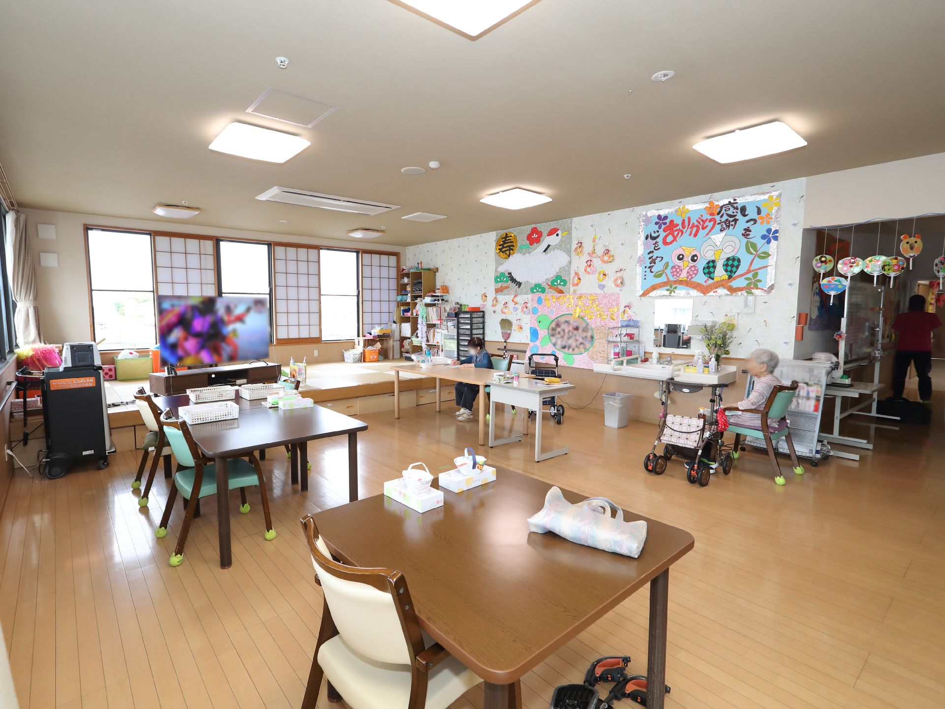 車椅子に乗って手を振る高齢女性と介助をする女性ヘルパー