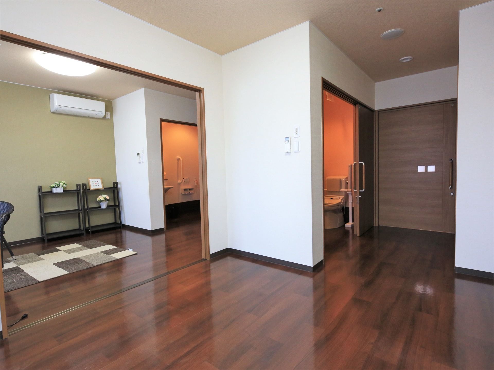 落ち着いた色合いのフローリングが敷かれた居室である。トイレの入り口には大きく開くスライド式ドアが設置されている。
