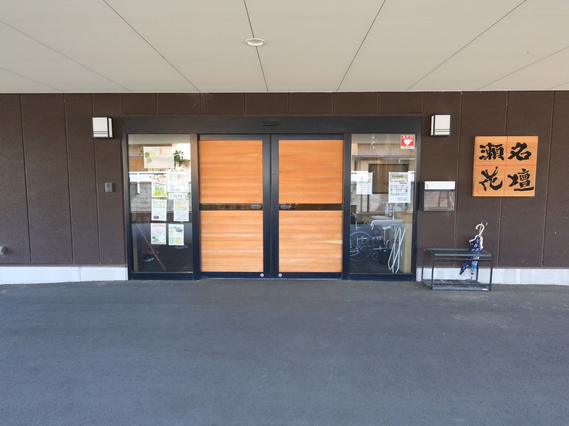 玄関には木目調の自動ドアが設置されている。ドアの両側に四角い照明がつけられていて、壁には筆文字の看板が設置されている。
