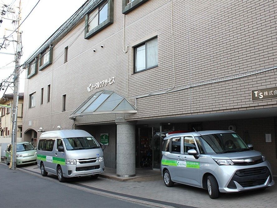 ブラウン系の外壁の３階建ての建物の外壁にはホーム名が書かれ、複数台のホームの車が周りに止まっている。