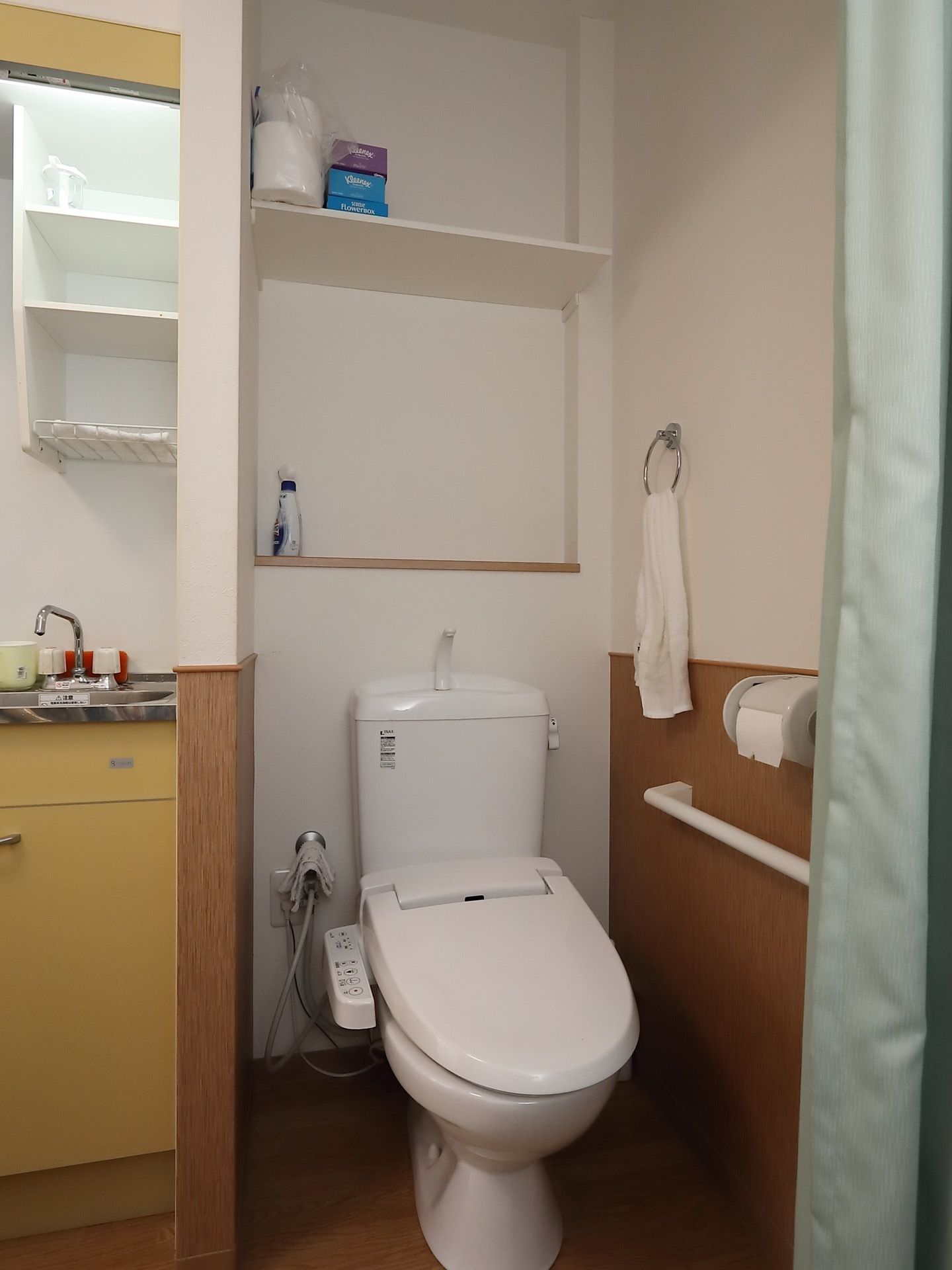 洋式トイレの個室内には、便器の背部に収納棚が2段設けられている。側面の壁にはタオル掛けや横手すりが備わっている。