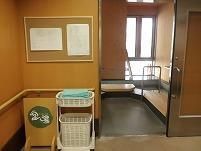 白衣を着た女性スタッフと高齢女性たちがソファを囲んで楽しそうに話している。スタッフは両隣の女性たちと手をつないでいる。