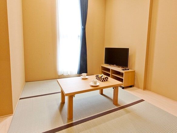畳敷きの小さな部屋の様子。縦長の窓とテレビ、テーブルが置いてある部屋