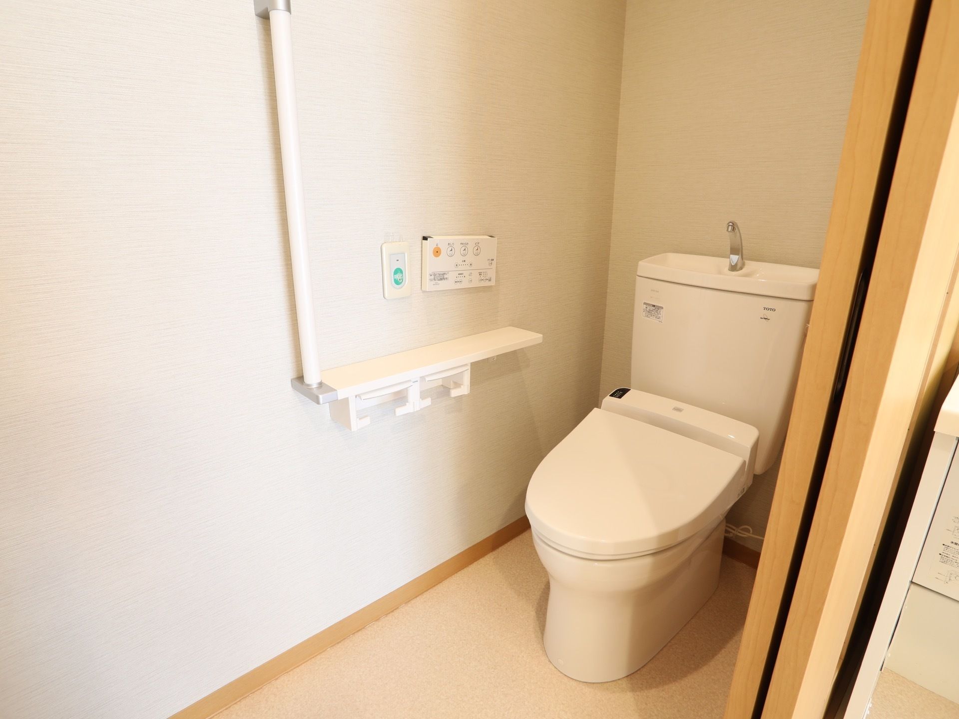 引き戸で仕切られた洋式トイレがある。壁には白い手すりのほか、洗浄ボタンや緊急用の通報装置も設置されている。