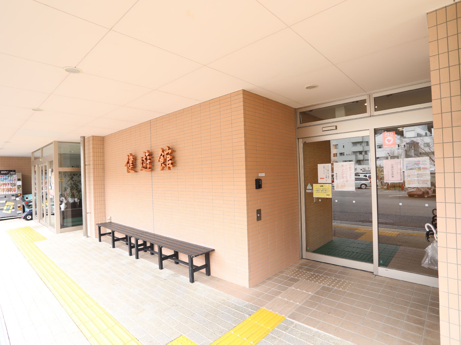 施設名の壁の立体文字の下にベンチが置かれた、建物の入口