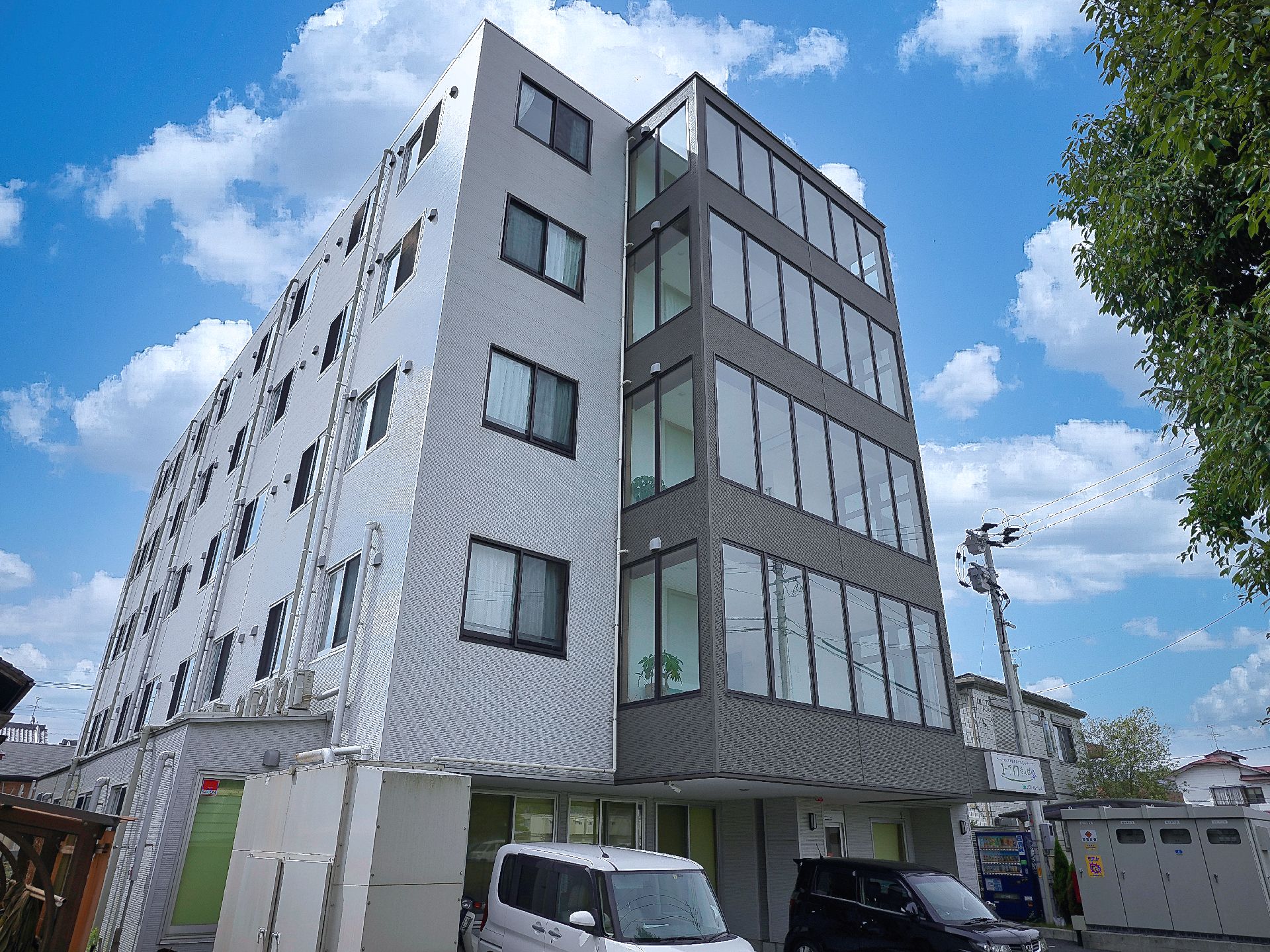 目の前に車が止まっている灰と黒の外観で５階建ての建物