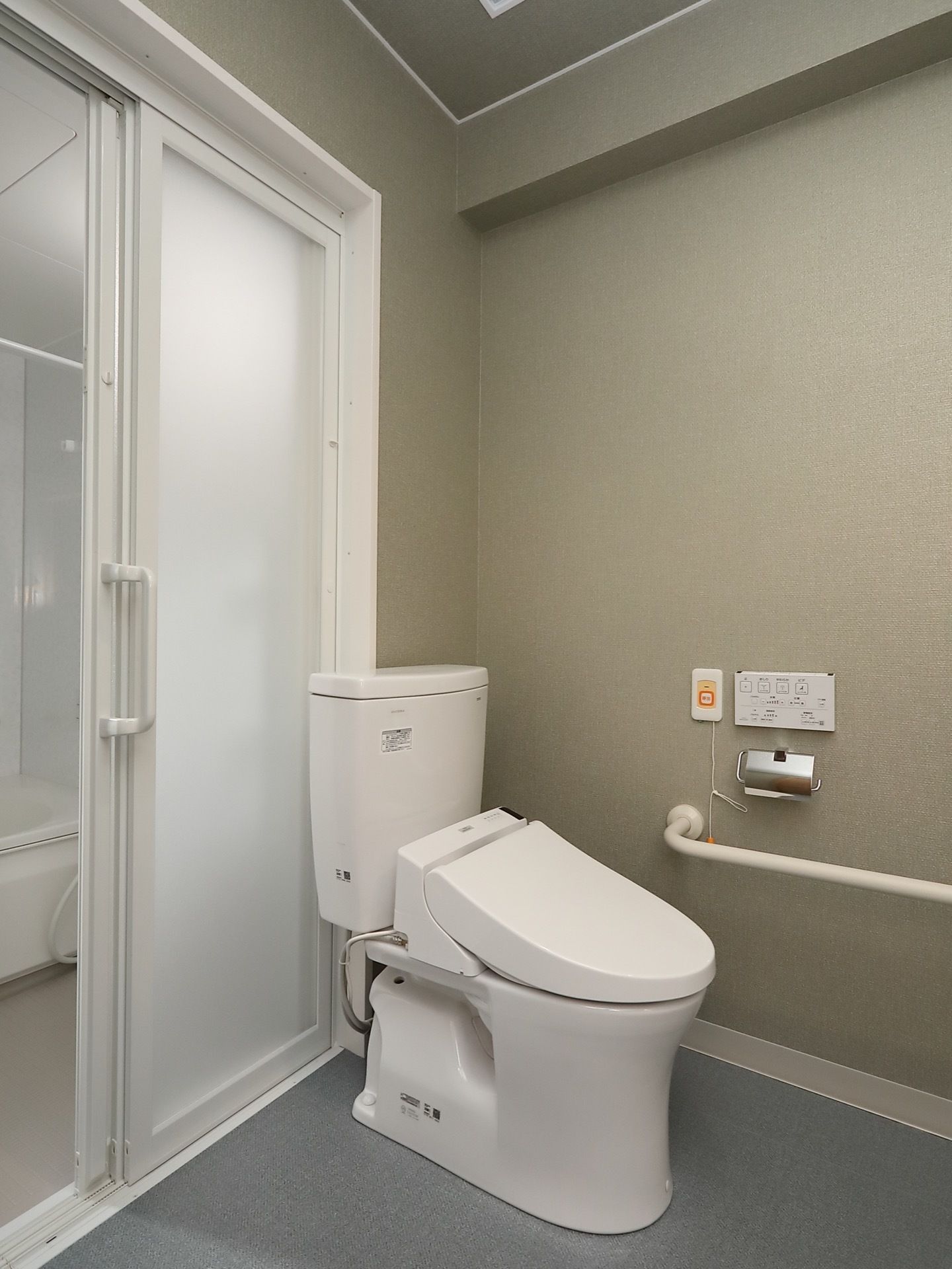 白と淡いグレーで統一されたモダンスタイルなトイレである。最新式の温水洗浄便座や手すり、ナースコールが完備されている。