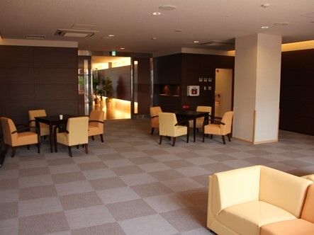 黄色い椅子の応接セットが複数置かれたラウンジ。カーペット敷きのフロアはモザイク柄。
