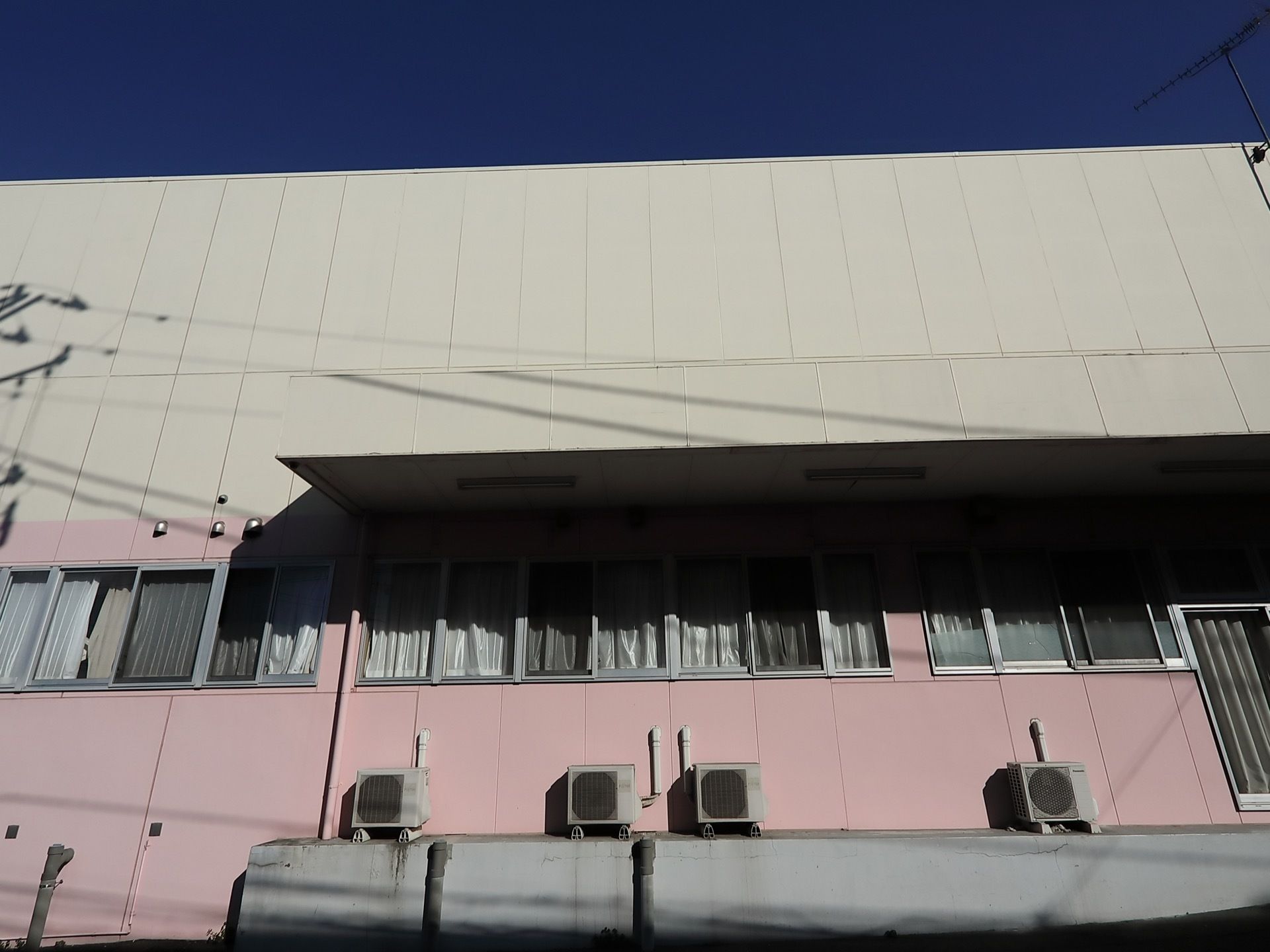 １階部分がピンク、２階部分が白の２階建ての大きな建物である。１階には窓が並んでおり、ひさしがついている。