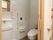 白い壁とブラウンの床の、天井の高い広いトイレがある。ドアはスライド式になっており、内部に洗面台と鏡が設置されている。